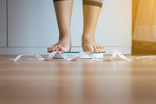 Someone standing on scales with tape measure on floor